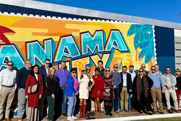 chamber leaders pose for photo in front of panama city beach mural