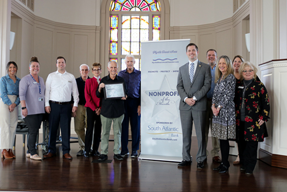 Brown Bradley and FPC Staff smile in front of Nonprofit of the Month banner.