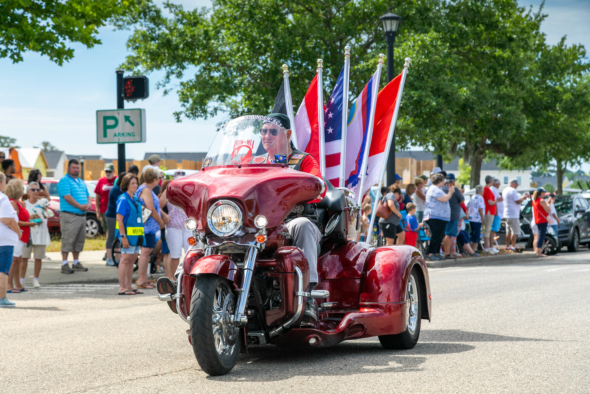 member of rolling thunder rides red motorcycle in front of parade crowd