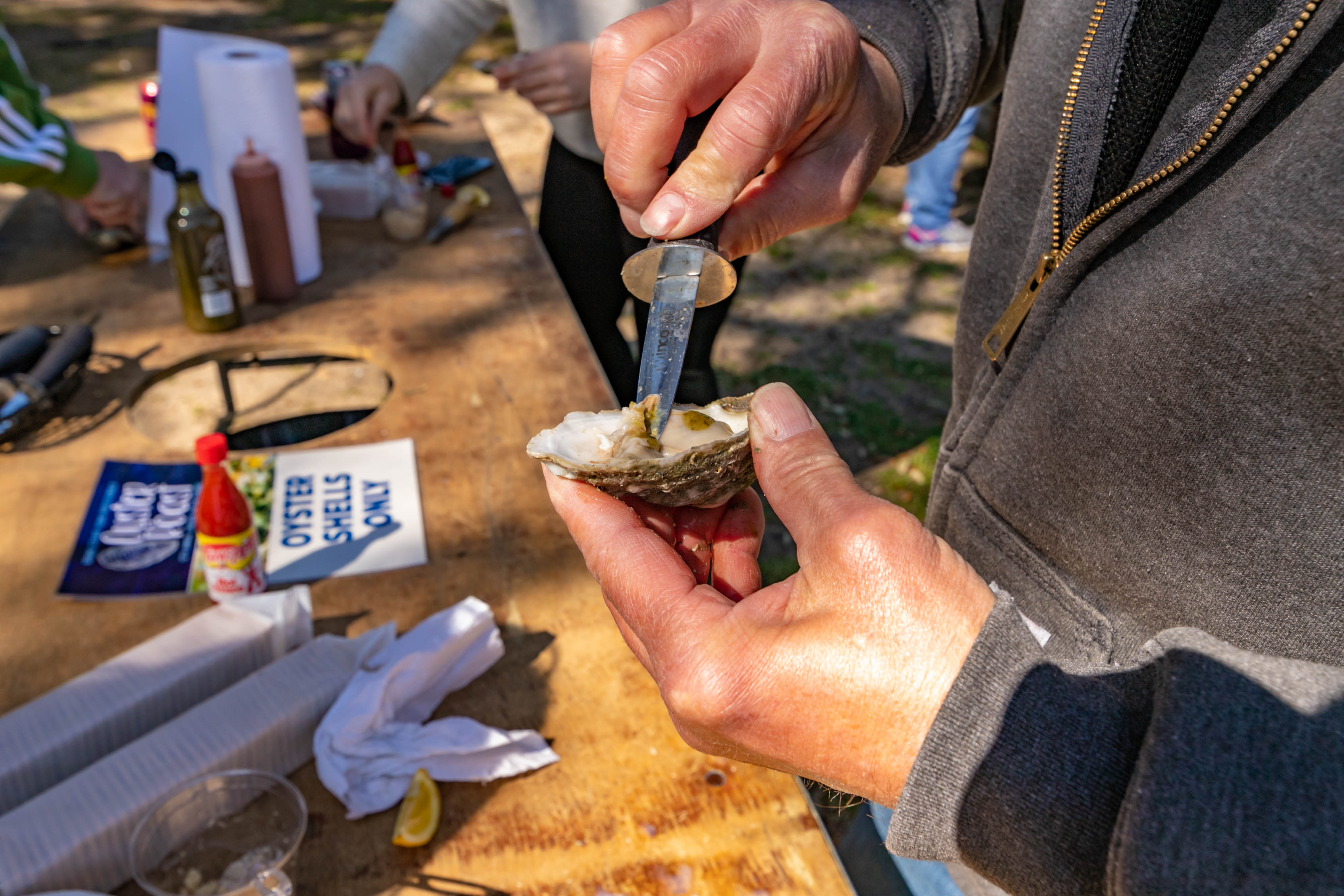 a person uses a knife to shuck an oyster