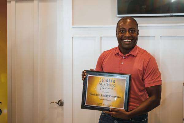 surfside realty employee smiles while holding leading business of the month plaque