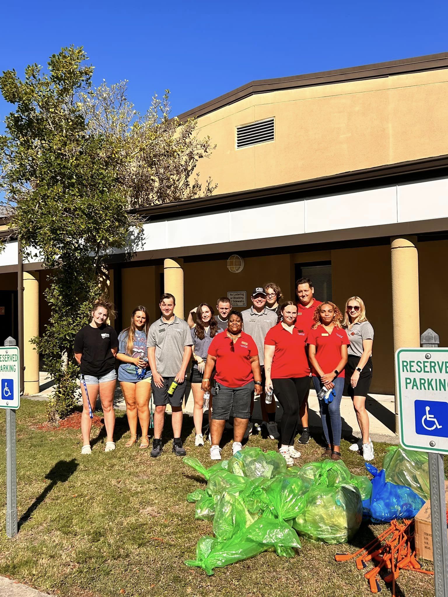KMBB Volunteers smile for a photo outside Pepper Geddings Recreation Center with a large pile of trash collected in green plastic bags in front of them.
