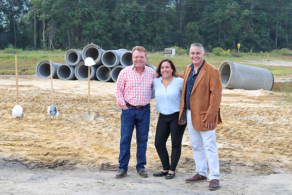 three people smiling at camera with dirt and shovels behind them